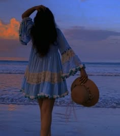 a woman in a blue dress is walking on the beach with her back to the camera