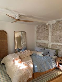 an unmade bed in a room with exposed brick walls and ceiling fan on the wall