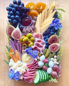 an arrangement of fruits, vegetables and meats on a platter with blue flowers