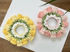 two crocheted flowers sitting on top of a piece of paper next to each other