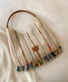 a white purse with multicolored fringes on the bottom and brown leather handle