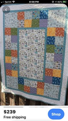 a quilt hanging on a fence in front of a wooden fence with an orange, blue and green patchwork design