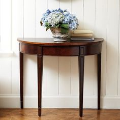 a wooden table with a flower pot on top of it next to a wall mounted clock