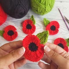 crocheted red flowers are being held by someone's hands with yarn in the background