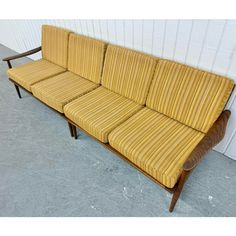 a yellow striped couch sitting in front of a white wall with a wooden armrest