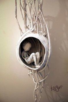 there is a sculpture in the shape of a baby's crib with branches hanging from it