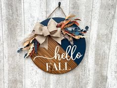 a wooden sign that says hello fall hanging on a wall with leaves and ribbons around it