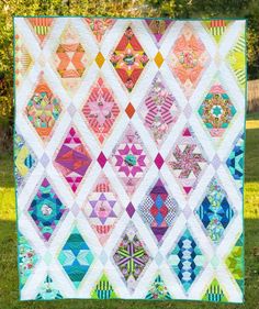 a colorful quilt on the grass with trees in the background