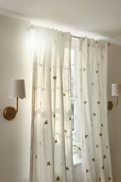 a white curtain with gold bees on it in front of a light fixture and window