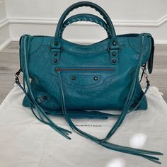 Balenciaga City Handbag This gorgeous teal blue-green City bag with classic hardware was purchased by me at the Balenciaga boutique inside Neiman Marcus. It has been gently used and in beautiful condition. The distressed leather is in amazing condition with the handles and piping/trim showing some wear. Tassels have all split (which means more tassels!:D). The interior looks almost new, immaculate with no stains, tears, odors, etc. The silver tag inside the bag still has the clear protective film on it. I own the City bag in several different colors and will list the other ones in the near future. DETAILS Color - Lagon Year - F/W 2012 Measurements - 15”x9.4”x5.5” Thanks for stopping by! Green City, Distressed Leather, Teal Blue, Piping, Neiman Marcus