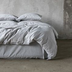 an unmade bed with white sheets and pillows on it in front of a concrete wall