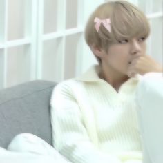 a person sitting on a couch with a pink bow in their hair and wearing a white sweater