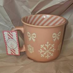 a pink coffee cup with snowflakes on it next to a small gift tag