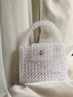 a white handbag sitting on top of a bed next to a sheer drapes