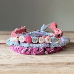 three bracelets with beads and letters on them sitting on top of a wooden table