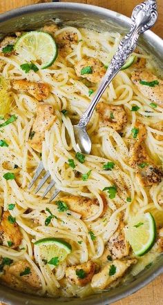 a skillet filled with chicken, noodles and lemons on top of a wooden table