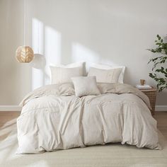 a bed with white linens and pillows in a room next to a potted plant