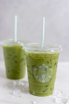 two green drinks with straws sitting on ice