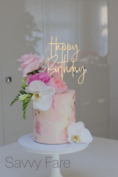 a pink and white cake with flowers on top that says happy birthday written in gold lettering