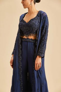 Editor's Note Navy blue georgette sharara with blouse and long jacket embroidered in tonal sequins, beadwork and crystals Color: Blue Fabric: Georgette and net Components: Sharara, blouse and jacket Occasion: Wedding guest Disclaimer: Product color may slightly vary due to photographic lighting sources or your monitor setting. Care: Dry Clean Only About the Designer Nitika Gujral’s journey with designing clothes started almost four decades back while she was still in high school and held her fir Sharara With Blouse, Sharara Blouse, Sharara Jacket, Navy Blue Sharara, Blue Sharara, Georgette Sharara, Designing Clothes, Blouse Yoke, Open Front Jacket