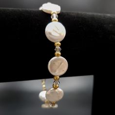 An elegant freshwater coin pearl clasp bracelet is ready to wear to a dressier event or be the perfect gift for someone lovely in your life. The bracelet includes flat, round 12 mm white pearl beads, clear bicone high-quality sparkly clear crystals, and delicate matte gold-colored glass spacer beads. The bracelet's clasp is a 14K gold-filled lobster clasp. The bracelet's stringing material is a high-quality, flexible gold-colored stringing wire. For added security, wire guards are placed on each Gold Pearl Bracelet, Pearl Clasp, Mother Of Pearl Jewelry, Clasp Bracelet, Coin Pearls, Birthstone Bracelets, White Freshwater Pearl, Clear Crystals, Bracelet Clasps