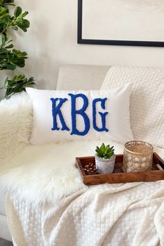 a white couch with a wooden tray on it and a pillow that says k b g