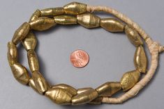 "A strand of handmade rustic brass beads from Ghana. Each is made one at a time - the Diamond Bicone shape is so interesting for tribal jewelry and rest comfortably on the neck. A favorite 21 beads 21\" of beads - 26\" overall 25x15x10mm on average 2-3mm hole" Antique Gold Polished Beads, Antique Large Gold Beads, Gold Jewelry Spacer Beads For Crafting, Antique Polished Gold Beads, Artisan Brass Jewelry With Large Beads, Antique Gold Beaded Necklaces With Large Beads, Vintage Gold Beaded Necklace With Wooden Beads, Gold Necklaces With Wooden Beads For Festivals, Vintage Gold Jewelry With Wooden Beads