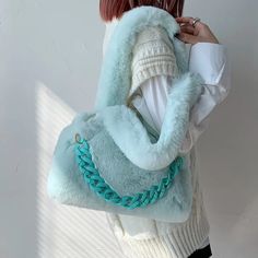 a woman with red hair wearing a white sweater and holding a blue handbag over her shoulder