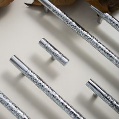 several silver pens are lined up on a white surface next to leaves and autumn leaves