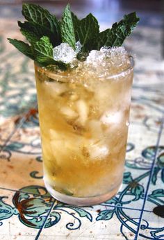 a close up of a drink on a table with ice and mint sprigs