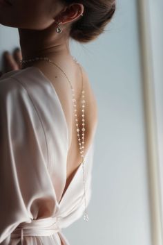 a woman in a white dress with pearls on her neck and back, wearing a long necklace