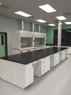 an empty laboratory room with white cabinets and black counter tops, green walls and lights