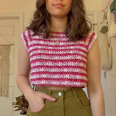 a woman wearing a red and white crochet top with her hands in her pockets