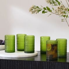 four green glass cups sitting on top of a table next to a vase with flowers in it