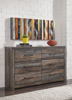 a wooden dresser sitting in front of a white brick wall with a painting on it