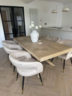 a dining room table with white chairs and a vase on top of the wooden table