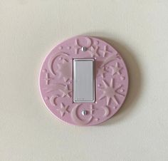 a pink light switch cover on a white wall with an ornate design in the middle