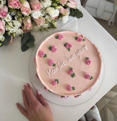 a pink frosted cake with roses on it and someone's hand next to it