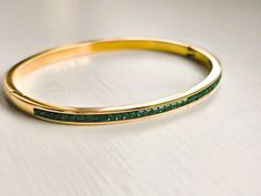 Introducing our 18K Gold Plated Bangle: sleek and elegant with AAA cubic green zircon setting. Perfect for layering, it adds a touch of sparkle to your wrist. Wear solo or stack for a bolder statement. This stunning solid bangle bracelet is super trendy and stylish! It's comfortable and lightweight. Looks great stacked or on its own! - - - D E T A I L S - - - Oval shape bangle * THICK plating of 18k Gold over Stainless steel * AAA green cubic zircon * Super high-quality & lightweight 15g * Size: Luxury Green Bangle In Fine Jewelry Style, Gold Emerald Jewelry With Channel Set, Green Bangle Crystal Bracelet For Formal Occasions, Green Crystal Bangle Bracelet For Formal Occasions, Channel Set Bangle Bracelets As Gift, Bangle Stacking, Layered Bangles, Bracelet Layering, Gold Plated Bangles