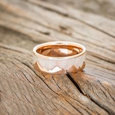 a wedding band with mountains on it sitting on top of a wooden table next to a piece of wood