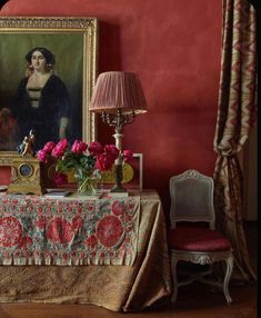 a room with red walls and a painting on the wall next to a table covered in flowers