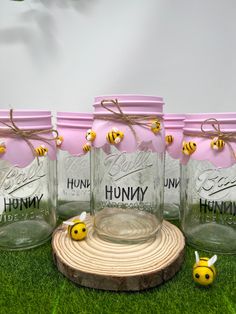 four mason jars with bees on them sitting in the grass next to a piece of wood