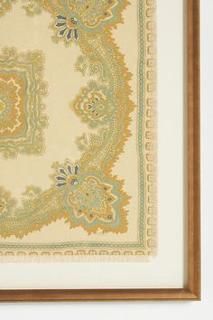 an ornately designed area rug hanging in a wooden frame on the wall next to a white wall