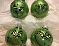 four green ornaments with yellow eyes and grin face drawn on them, sitting on a sheet of paper