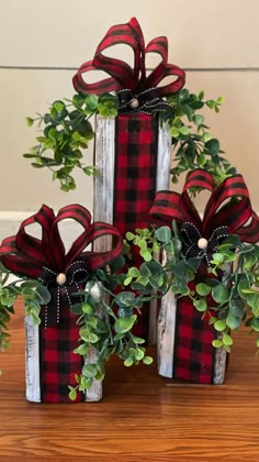 three wrapped presents with red and black bows are sitting on a wooden table next to greenery