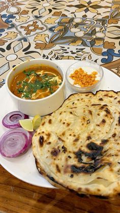 a white plate topped with food next to a bowl of soup and a tortilla