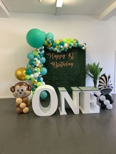 a happy 1st birthday sign with balloons and stuffed animals in front of the letters one