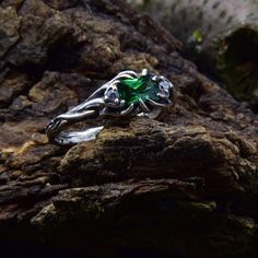 a green ring sitting on top of a rock next to a tree branch with leaves