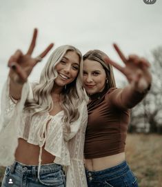 two beautiful young women standing next to each other holding their hands up in the air