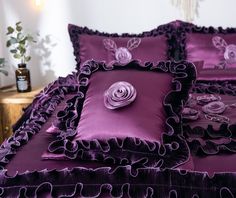 a bed with purple comforters and pillows on top of it, next to a potted plant